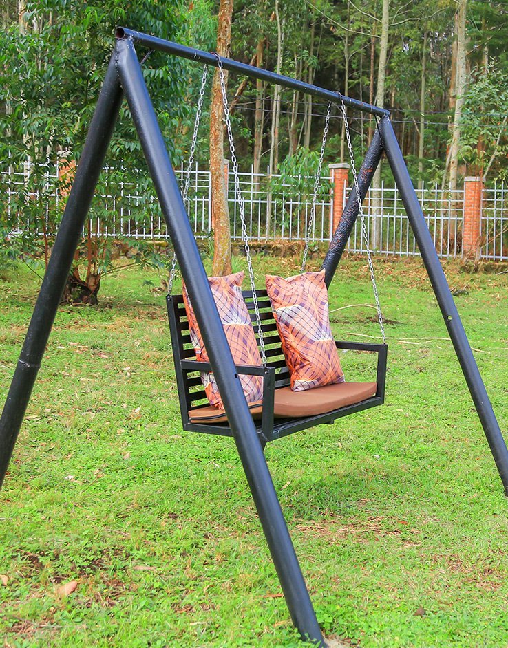 Black metal garden swing on a lawn with trees and a white fence behind it