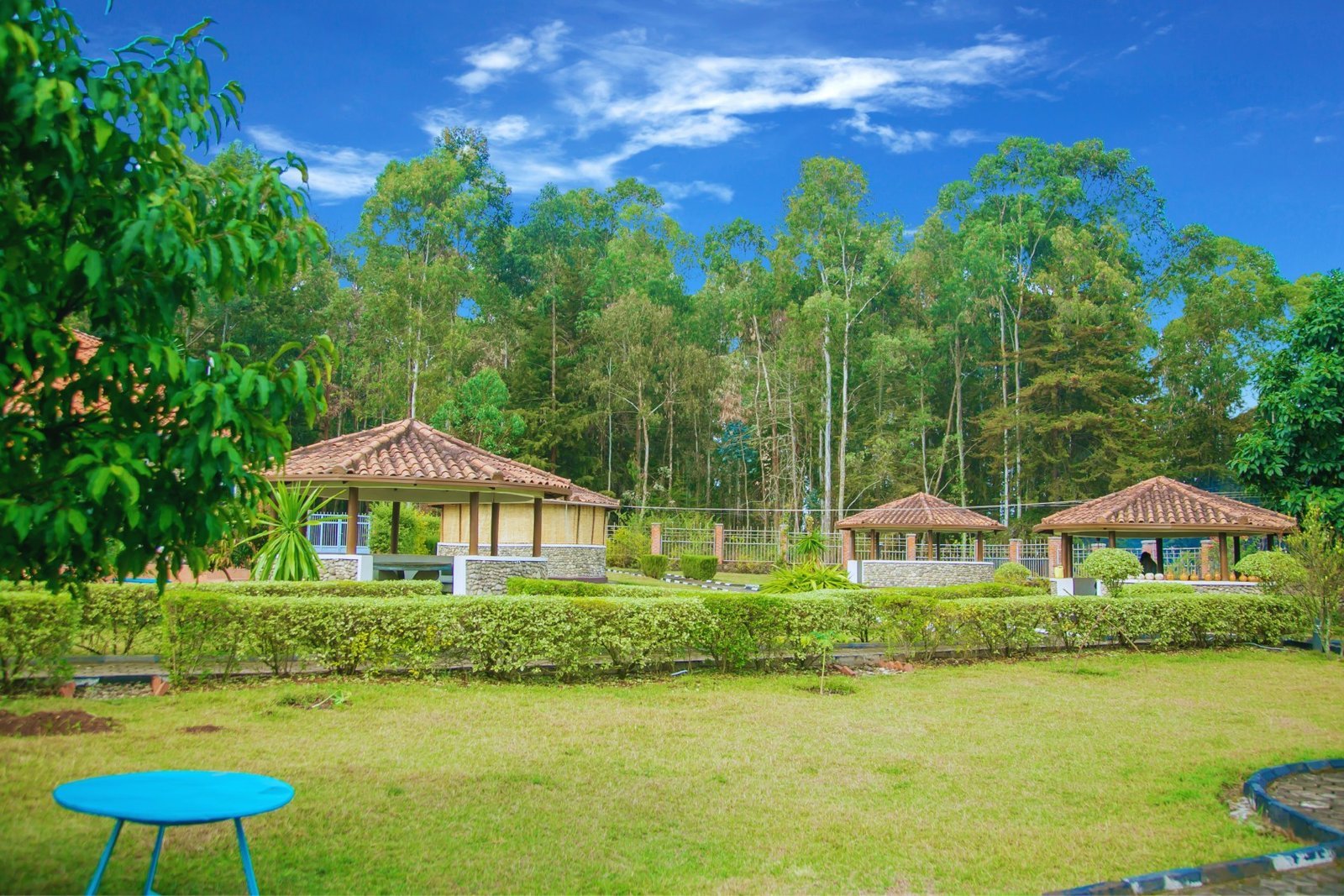 Landscaped gardens with stone gazebos, eucalyptus trees and a clear blue sky at Karisimbi Cave Resort