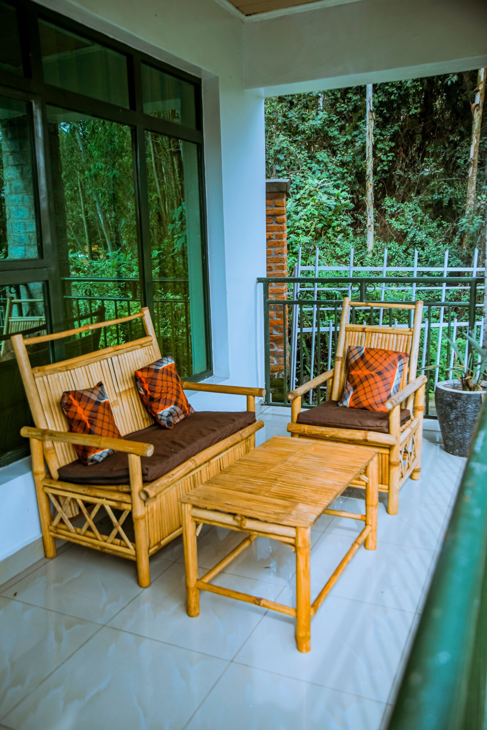 Bamboo armchairs and a coffee table on a tiled balcony overlooking green forest